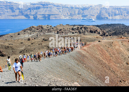 Santorini, Erinia Bay, Nea Kameni. I turisti a piedi al bordo del vulcano dal porto lungo ruvida percorso roccioso attraverso il paesaggio desolato sotto il sole caldo. Foto Stock