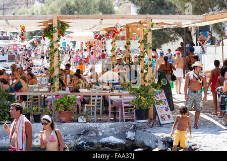 Santorini, Thirasia. Korfos, Cadouni, caffetteria, ristorante sul litorale. Affollate di turisti di mangiare a tavoli e sedie. Sole brillante, metà giornata. Foto Stock