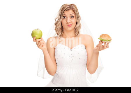 Giovane sposa tenendo un Apple in una mano e un hamburger in altri isolati su sfondo bianco Foto Stock