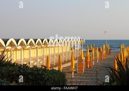 Colorate scatole di balneazione su una spiaggia in righe con alcuni ombrelloni da spiaggia Foto Stock