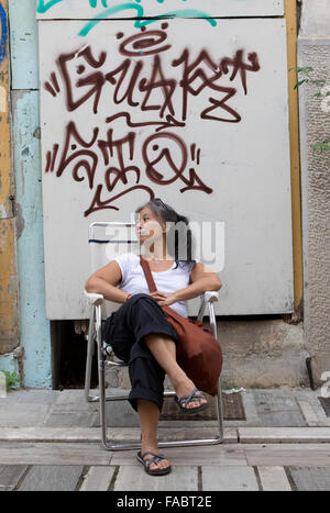 Turista femminile in appoggio su una sedia sotto Graffiti in Nauplia,Grecia. Foto Stock