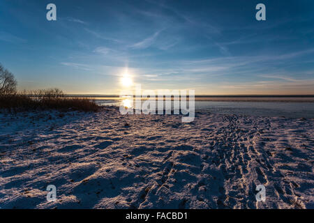 Sun riguarda l'orizzonte sulla costa d'inverno, che viene riflessa dalla neve, acqua e ghiaccio. Foto Stock