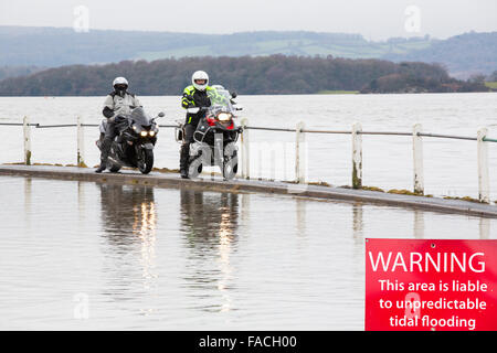 Bikers viaggio attraverso le acque di esondazione su strada a Storth sul Kent Estuary in Cumbria, Regno Unito, durante il mese di gennaio 2014 storm surge Foto Stock