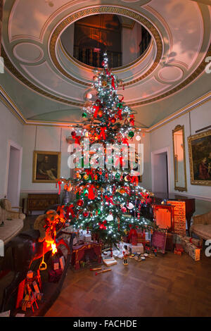 Regno Unito, Inghilterra, Cheshire, Knutsford, Tatton Hall, il grande albero di Natale decorato con presenta qui di seguito nella Hall per scale Foto Stock