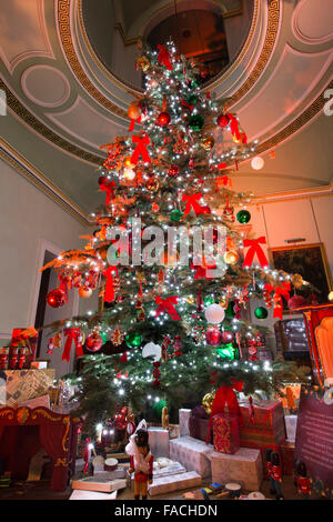 Regno Unito, Inghilterra, Cheshire, Knutsford, Tatton Hall, il grande albero di Natale decorato con presenta qui di seguito nella Hall per scale Foto Stock