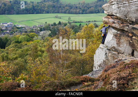 Un rocciatore sul bordo Froggatt nel Peak District, Derbyshire. Colore di autunno in alberi di seguito. Foto Stock