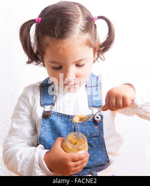 Ritratto di felice ragazza di mangiare un frutto giara di pappe per bambini. Isolato su sfondo bianco Foto Stock