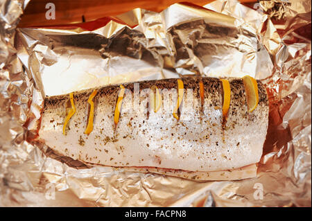 Salmone intero essendo preparato per la cottura con il limone e le erbe aromatiche in lamina Foto Stock