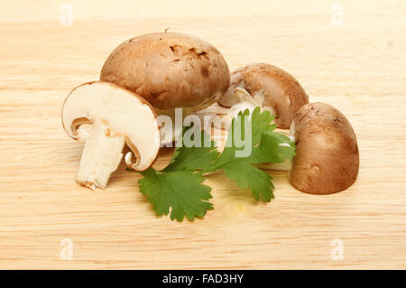 Intero e fette di funghi castagne con coriandolo su una tavola di legno Foto Stock