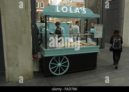 Vista, verso Brushfield Street, donna oltrepassando Lola's tortine in stallo verso gli uomini parlare, Old Spitalfields Market, Londra Foto Stock