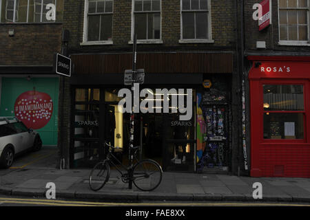 Vista della bicicletta fissata un lampione di fronte scintille negozio di abbigliamento accanto alla Rosa's Cafe Thai, Hanbury Street, Londra, E1, Regno Unito Foto Stock