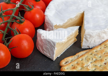 Brie formaggio a pasta morbida con cracker e pomodori in un grigio ardesia bordo. Messa a fuoco selettiva Foto Stock