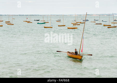 Un uomo che rema con una piccola barca a vela dinghy in mare al largo della costa di Seaview Isle of Wight REGNO UNITO su un nuvoloso giorno Foto Stock
