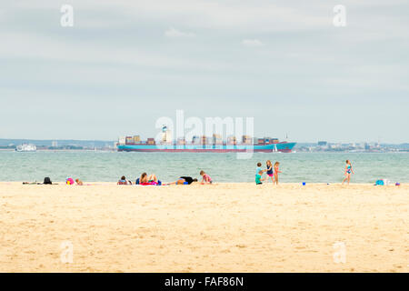 La gente a prendere il sole sulla spiaggia a Ryde Isle of Wight UK con un contenitore grande nave passando in mare Foto Stock