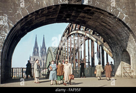 Passanten flanieren unter dem Brückenportal der Hohenzollernbrücke in Köln mit Blick auf den Dom, Deutschland 1950er Jahre. I passanti sotto il ponte porta del ponte Hohenzollernbruecke a Colonia con vista della cattedrale, Germania degli anni cinquanta. Foto Stock