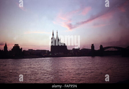 Abendstimmung mit der Silhouette von Rathaus, Dom und der im Wiederaufbau befindlichen Kirche Groß San Martin am Rhein in Köln, Deutschland 1950er Jahre. Atmosfera serale con silhouette del municipio, la cattedrale e la chiesa al lordo di San Martin in ricostruzione al fiume Reno a Colonia, Germania degli anni cinquanta. Foto Stock