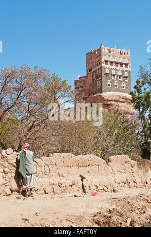 Medio Oriente: un uomo yemenita appoggiata contro un muro di pietra orologi il Dar al Hajar, Dar al Hajar, il Rock Palace, il Royal Palace, simbolo iconico dello Yemen Foto Stock