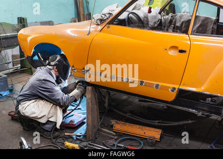 Carrozziere che ripristina un classico auto VW Karmann Ghia. I lavori di saldatura alla carrozzeria del veicolo. Foto Stock