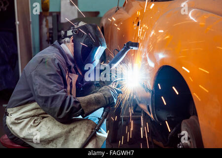 Carrozziere che ripristina un classico auto VW Karmann Ghia. I lavori di saldatura alla carrozzeria del veicolo. Foto Stock