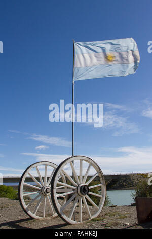 Bandiera dell'Argentina soffiando nel vento all aperto con ruote di carri contro il cielo blu in Patagonia. Foto Stock