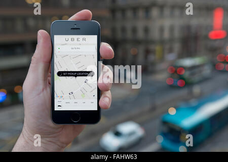 Un uomo utilizza il taxi Uber app sullo smartphone mentre si fermò in un alto edificio che si affaccia su una strada trafficata (solo uso editoriale) Foto Stock