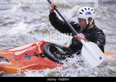 Uomo che indossa un casco bianco che va in kayak arancione attraverso acque ruvide, nel parco di Burrs Country a Bury lancashire uk Foto Stock