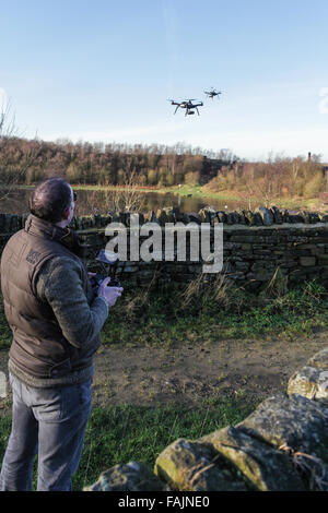 Uomo esterno che controlla il drone dal telefono cellulare o dallo schermo del tablet. Due droni in vista volare. Foto Stock