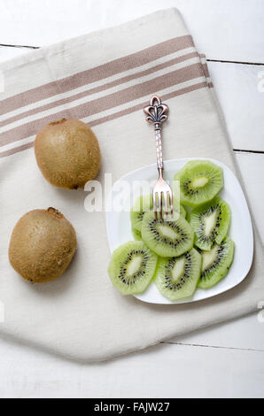 Fette di kiwi sulla piastra di bianco su bianco tavolo in legno Foto Stock