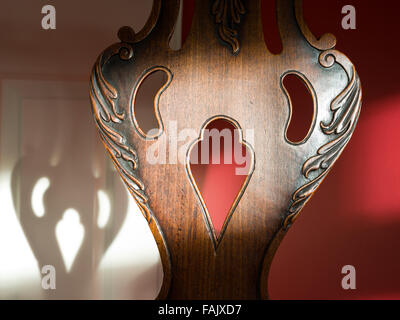 Antiquariato del legno schienale con tagliare la decorazione a forma di un cartone animato in faccia. Corrispondente faccia ombra in background. Foto Stock