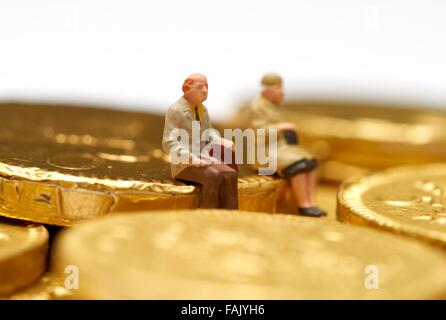 Miniatura gente seduta sul cioccolato monete di denaro Foto Stock