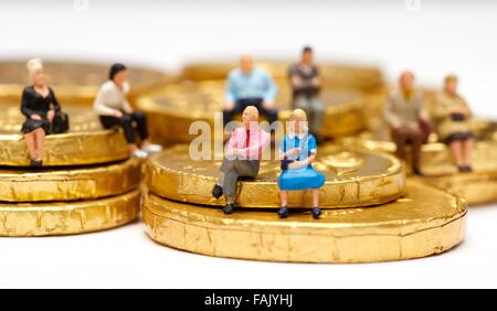 Miniatura gente seduta sul cioccolato monete di denaro Foto Stock