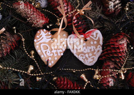 Due biscotti dolci a forma di cuore in ghirlanda di Natale tra coni e brillare campane Foto Stock