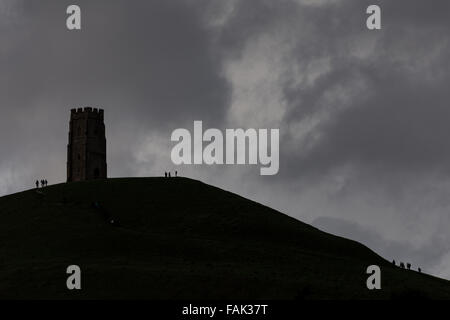 Glastonbury, Somerset, Regno Unito. Il 31 dicembre, 2015. Centinaia di persone che fanno il pellegrinaggio Vigilia di Capodanno al top di Glastonbury Tor nonostante i forti venti e minaccia di docce a pioggia. Molte più persone rimarranno sul fianco di una collina che si affaccia sulla pianura alluvionale del Somerset per vedere la prima alba del 2016. Credito: Wayne Farrell/Alamy Live News Foto Stock