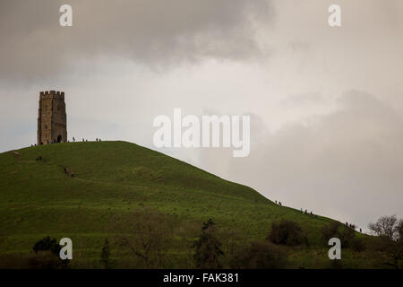 Glastonbury, Somerset, Regno Unito. Il 31 dicembre, 2015. Centinaia di persone che fanno il pellegrinaggio Vigilia di Capodanno al top di Glastonbury Tor nonostante i forti venti e minaccia di docce a pioggia. Molte più persone rimarranno sul fianco di una collina che si affaccia sulla pianura alluvionale del Somerset per vedere la prima alba del 2016. Credito: Wayne Farrell/Alamy Live News Foto Stock