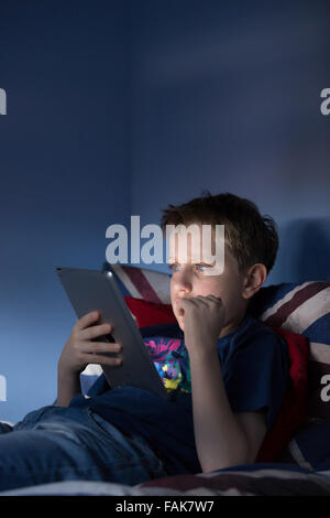 Un ragazzo seduto in ritardo nella sua camera da letto guardando internet sconvolto per ciò che egli è visto Foto Stock