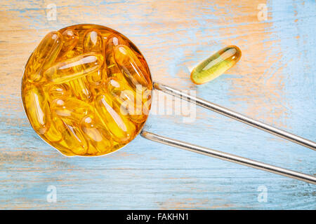 Olio di pesce supplemento capsule in un metallo coppa di misurazione di un dipinto di grunge di legno di legno - vista superiore Foto Stock