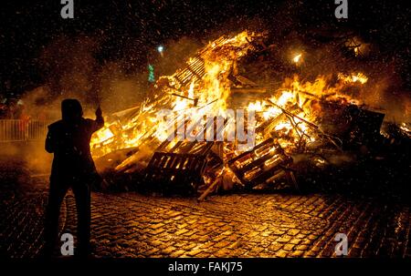 Biggar, South Lanarkshire, Scotland, Regno Unito. Il 31 dicembre, 2015. Continuando una tradizione che risale a centinaia di anni la spettacolare hogmanay falò in Biggar's High Street è stata accesa alle 21.30 su Hogmanay. Il fuoco, la dimensione di una casa a due piani, è stato illuminato dai residenti locali Christine Smith guardato da una folla di diverse migliaia di persone da Biggar e le aree circostanti. Un uomo lancia una torcia ardente sul fuoco. Credito: Andrew Wilson/Alamy Live News Foto Stock