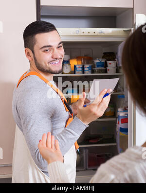 La casalinga che mostra frigorifero rotto per sorridere repairman Foto Stock