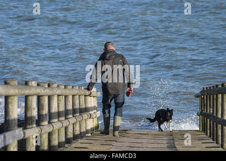 L uomo e il suo cane - un uomo e il suo cane a camminare su una passerella di legno sull'estuario del Tamigi Foto Stock