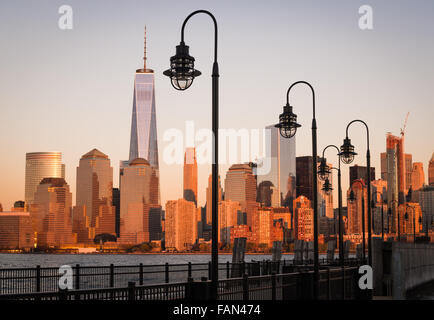 Un molo abbandonati con lampade di via guarda attraverso il Fiume Hudson fino alla parte inferiore dello skyline di Manhattan che riflette il tramonto dorato. Foto Stock