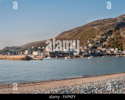 Una vista attraverso il fiume Mawddach estuary verso Barmouth porto e città con barche ormeggiate e pescatori sulla parete del mare. Foto Stock