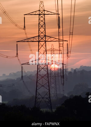 Elettricità tralicci stagliano contro il sole di setting in Devon Foto Stock