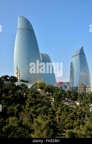 Guardando le torri a fiamma a Baku, capitale dell'Azerbaigian, sotto il sole con alberi in primo piano. Foto Stock
