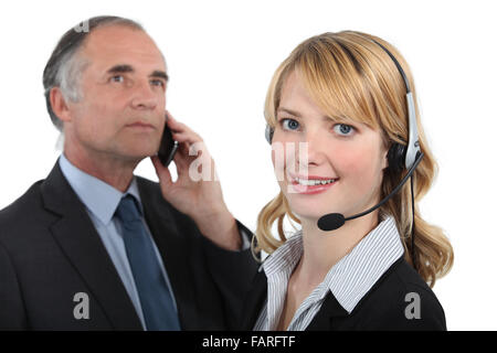 La donna in un auricolare accanto a un uomo con un telefono cellulare Foto Stock