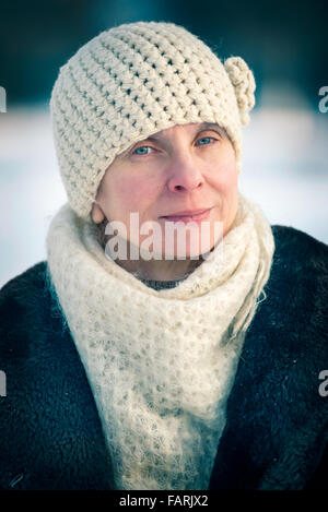 Un inverno ritratto di un senior adulto donna che indossa un cappello di lana e una sciarpa con un background di neve Foto Stock