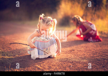 Bambina giocando nella sporcizia con un bastone Foto Stock