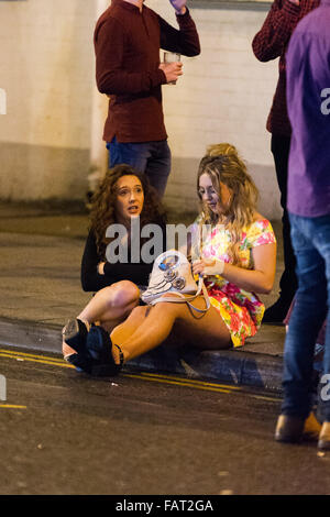 Nella foto: due donne siedono sul cordolo. Re: Capodanno a Cardiff, nel Galles del Sud, Regno Unito. Prime ore di venerdì 1 gennaio 2016. Foto Stock