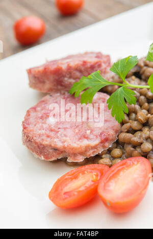 Piatto di lato di sausagecotechino e le lenticchie con il prezzemolo e il pomodoro sweet Foto Stock
