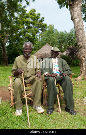 Coppia di anziani del villaggio seduto sul fatto in casa sedie sul villaggio verde, Kenya. Foto Stock