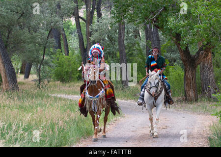 Guerrieri in abiti Comanche cavalcando i loro cavalli su un sentiero attraverso la foresta, New Mexico Foto Stock